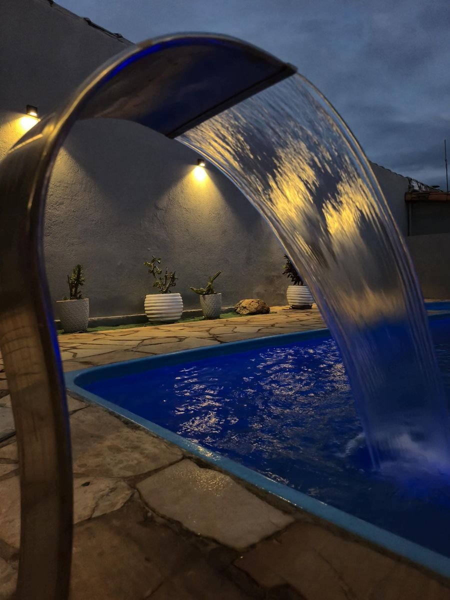 Cascata de inox ligada com o reflexo das arandelas na lâmina de água e a piscina iluminada em azul